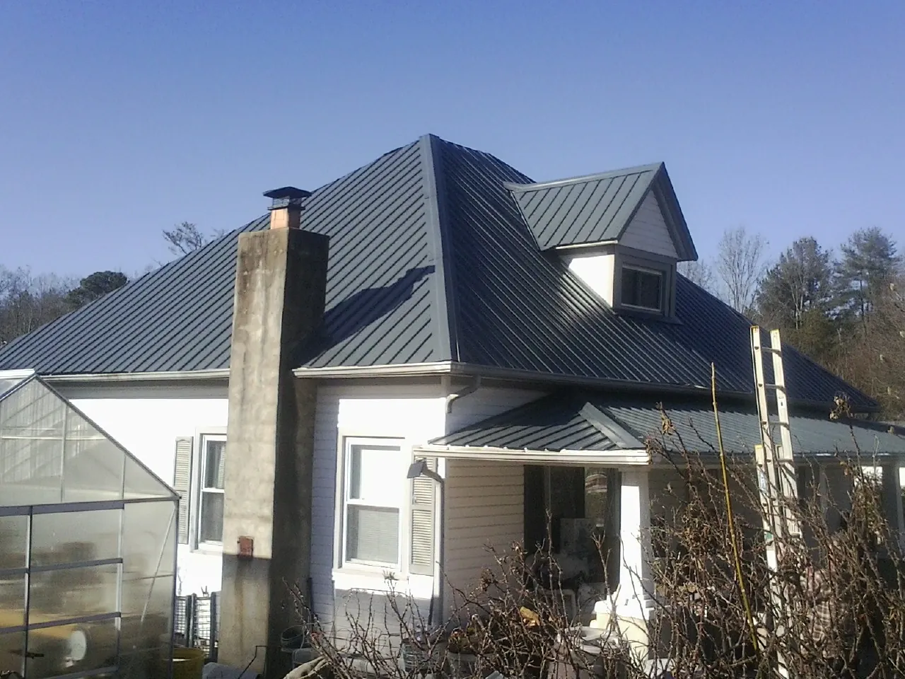 Dark blue standing seam metal roof on a white farmhouse with dormer — Slate & Tile Roof Repair by Roofing Brothers in Summerland