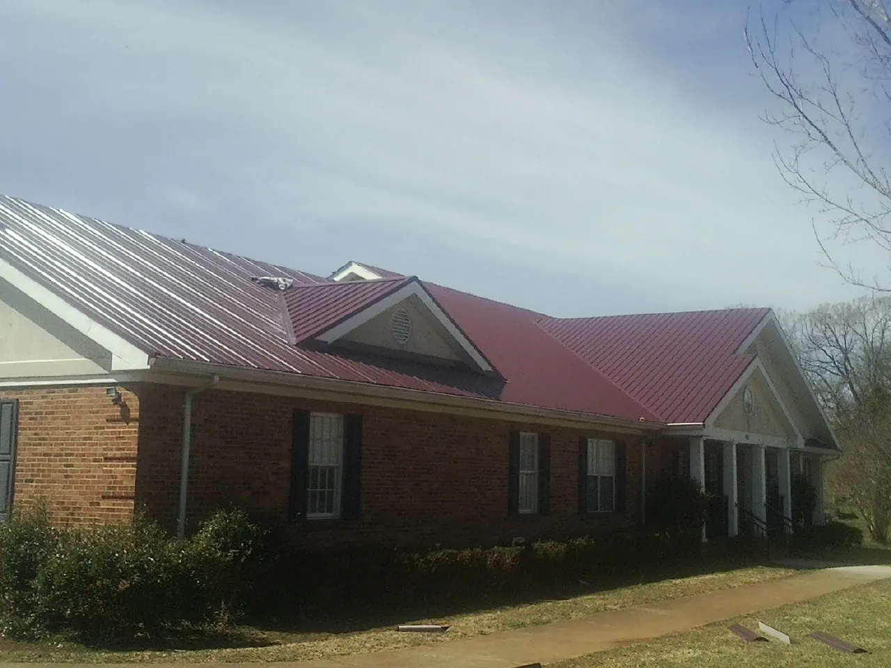 Red metal roof with gabled entries on a long brick building, from a Hail Damage Roof Repair job in Summerland