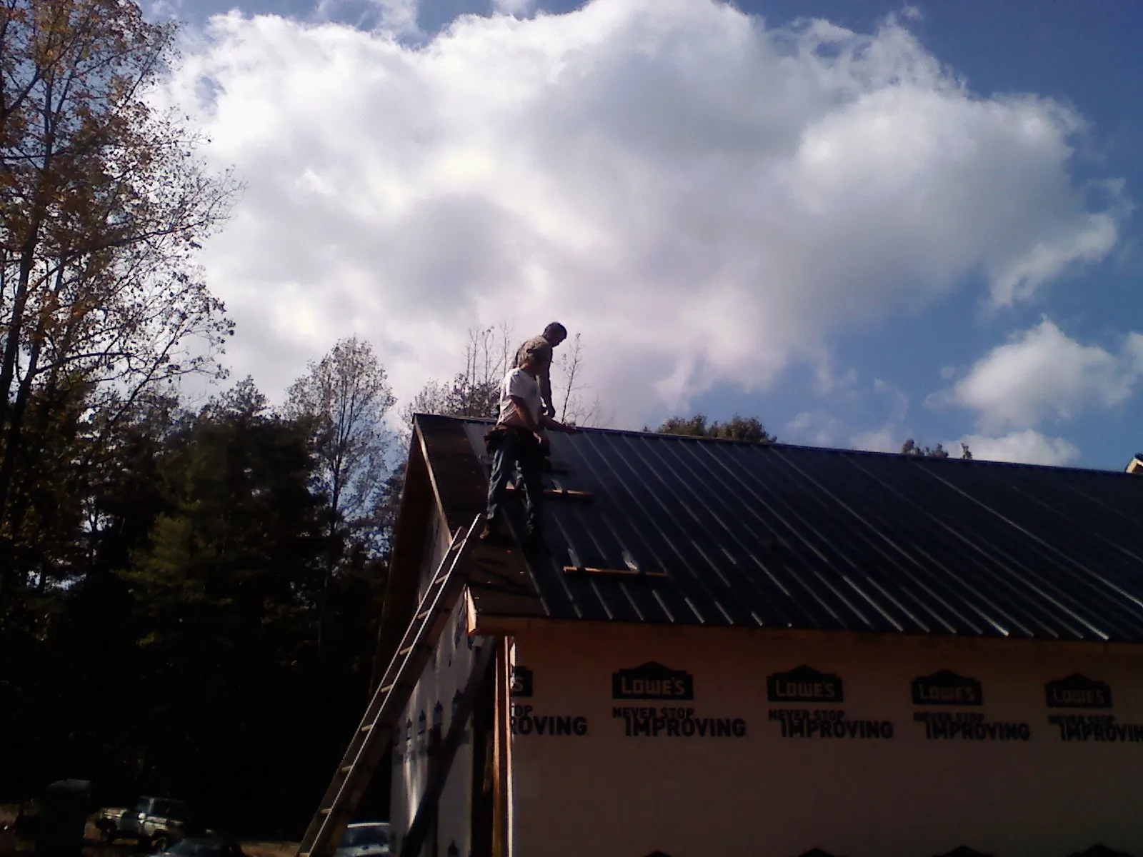 Roofer fastening dark metal panels high against a cloudy sky, from a Roof Inspection job in Summerland
