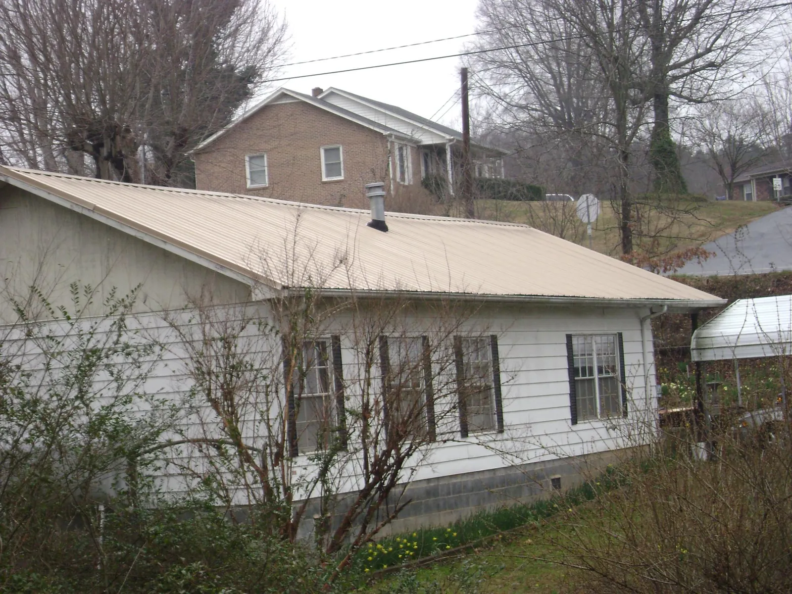 Tan metal roof on a white sided house set into a hillside — Commercial Roofing by Roofing Brothers in Summerland